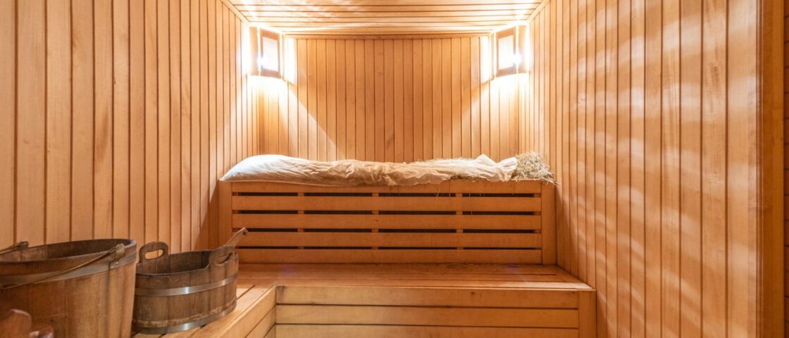 Wooden sauna cabin interior with tiered benches, water buckets and a heater