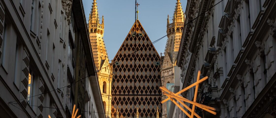 The diamond-patterned tiled roof of St Stephen's Cathedral in Vienna seen down a narrow street at sunset