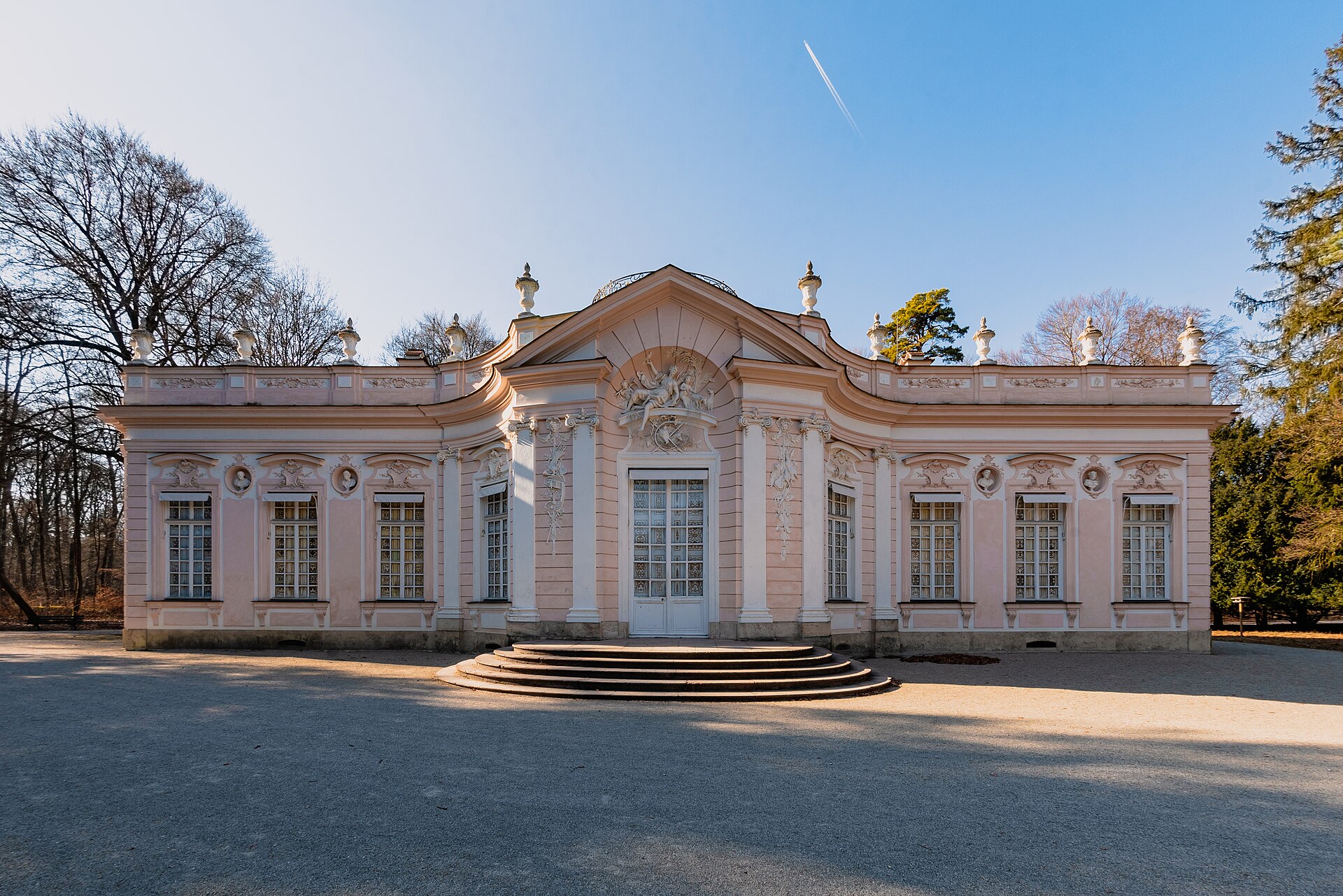 Nymphenburg Palace Munich: Complete Visitor Guide (2026) 3 Amalienburg’s pink facade and white sculpted ornament face a gravel forecourt in Nymphenburg Palace Park, surrounded by trees.