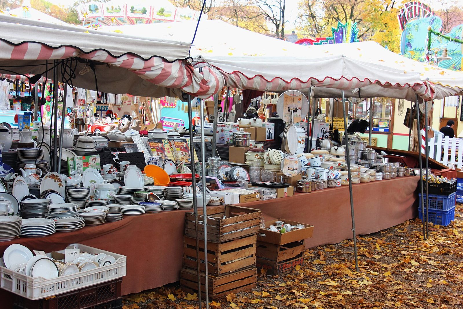Auer Dult: Munich's Traditional Fairs and Markets 1 A crockery stall stacked with plates, bowls and jugs under an awning, autumn leaves on the cobbles