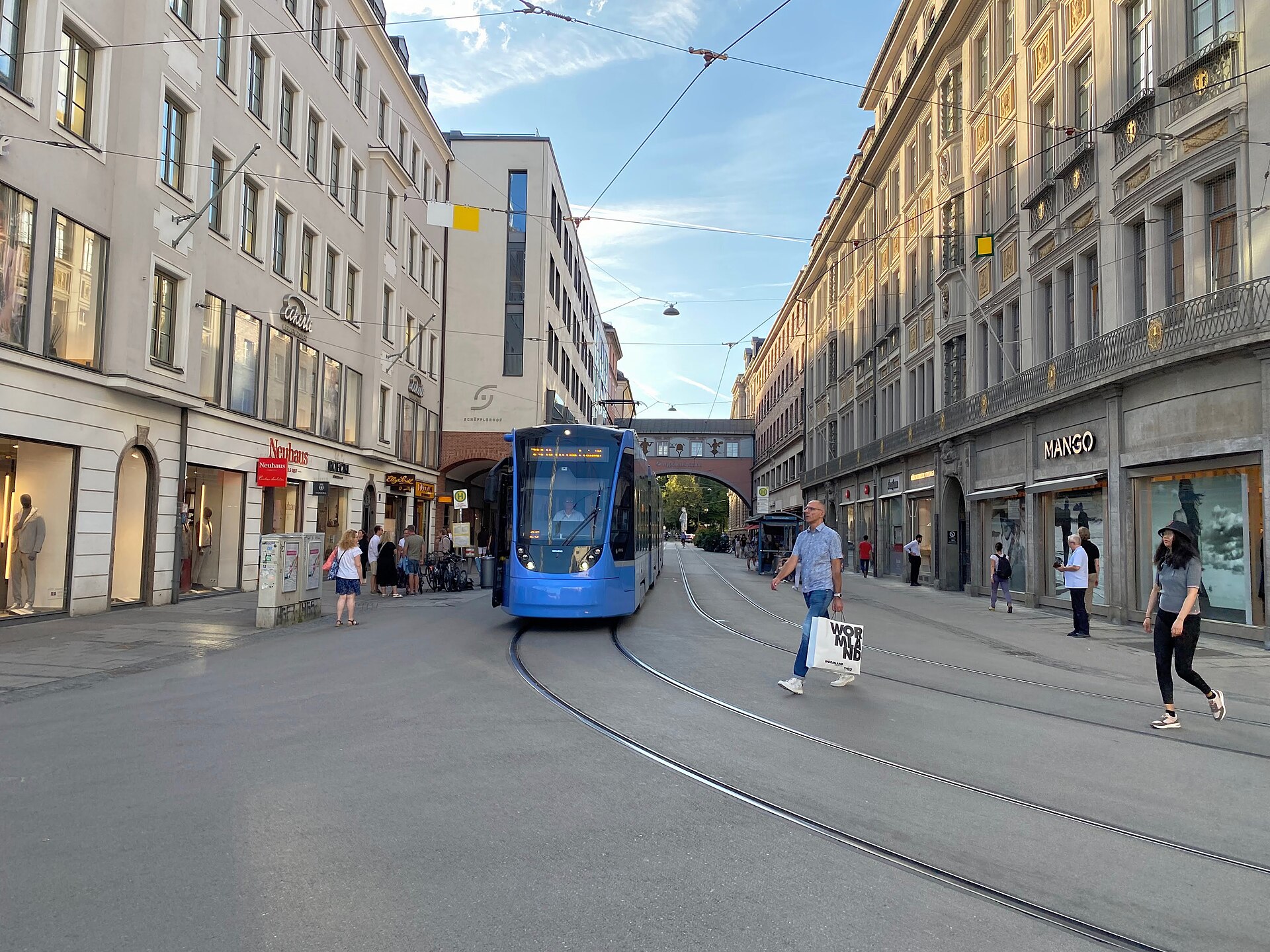 Getting Around Munich: Complete Transport Guide 3 A blue Munich tram follows curved tracks along Maffeistrasse as pedestrians cross between rows of shops.