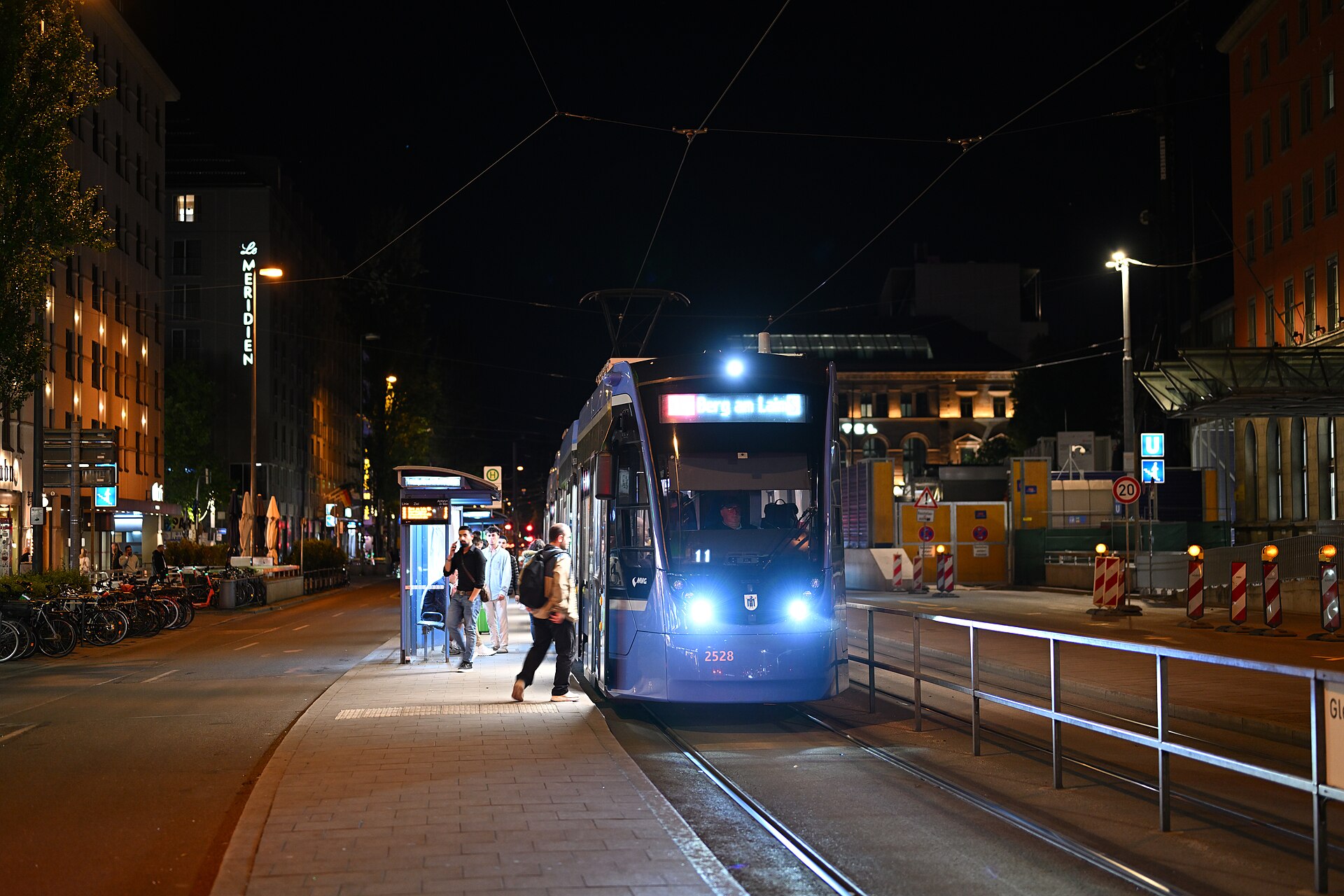 Getting Around Munich: Complete Transport Guide 9 A blue Munich tram stops beside passengers at Hauptbahnhof Sued beneath overhead wires and the dark night sky.