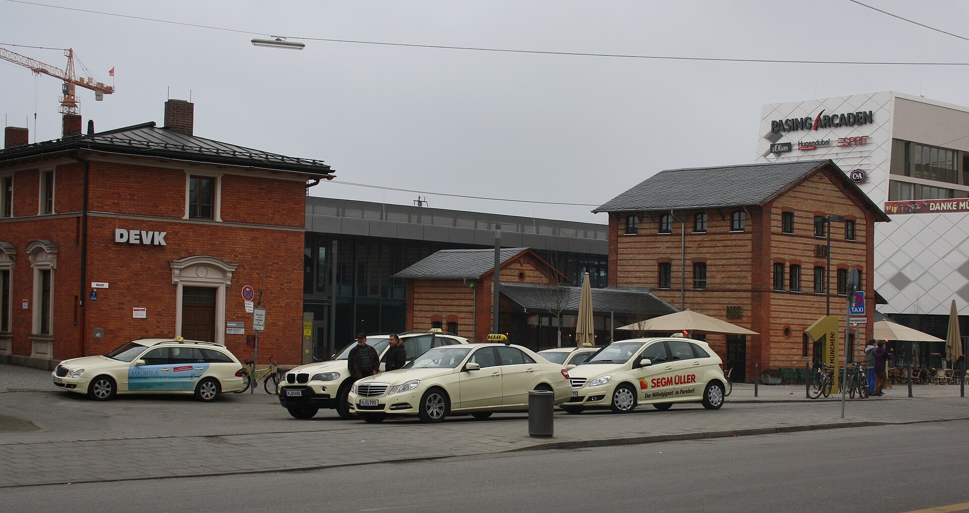 Getting Around Munich: Complete Transport Guide 8 Cream taxis wait outside Munich Pasing station beside brick buildings and an outdoor cafe.