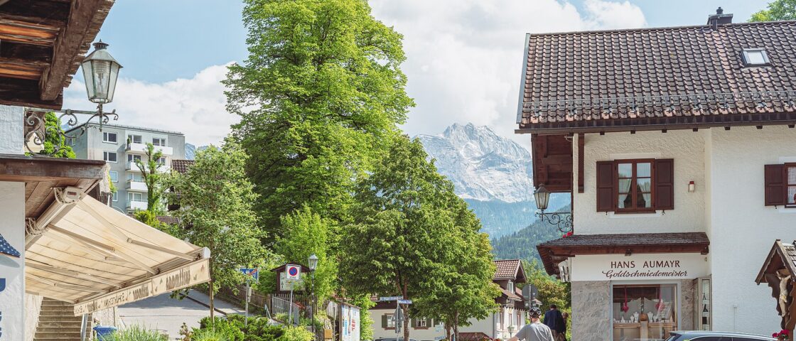 A cyclist walks along Ludwigstrasse in Garmisch-Partenkirchen, with traditional houses and a rocky mountain rising behind.