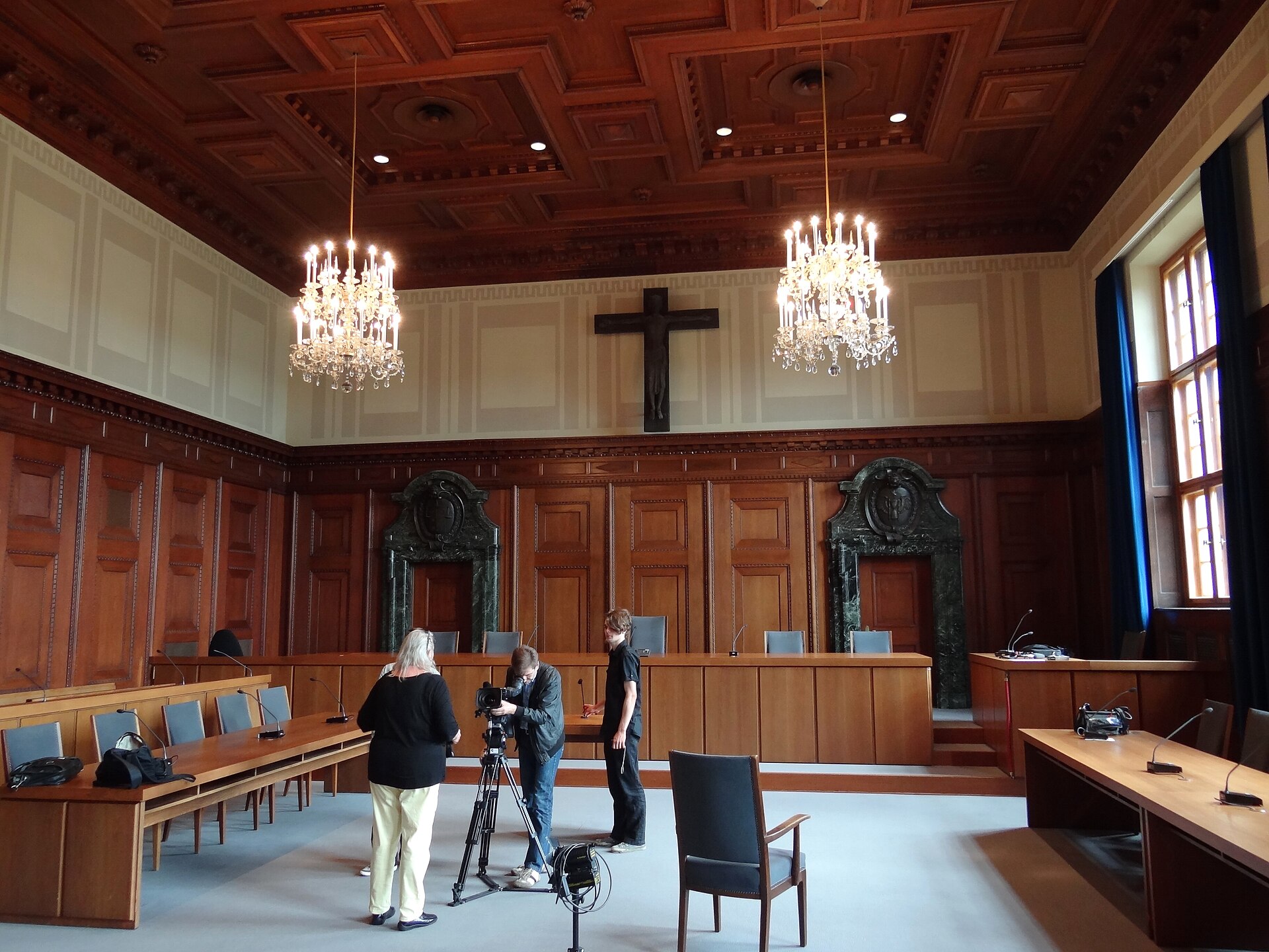 Nuremberg Day Trip from Munich: Complete History and Food Guide 1 A film crew sets up a camera among wooden benches beneath chandeliers in Nuremberg’s wood-paneled Courtroom 600.