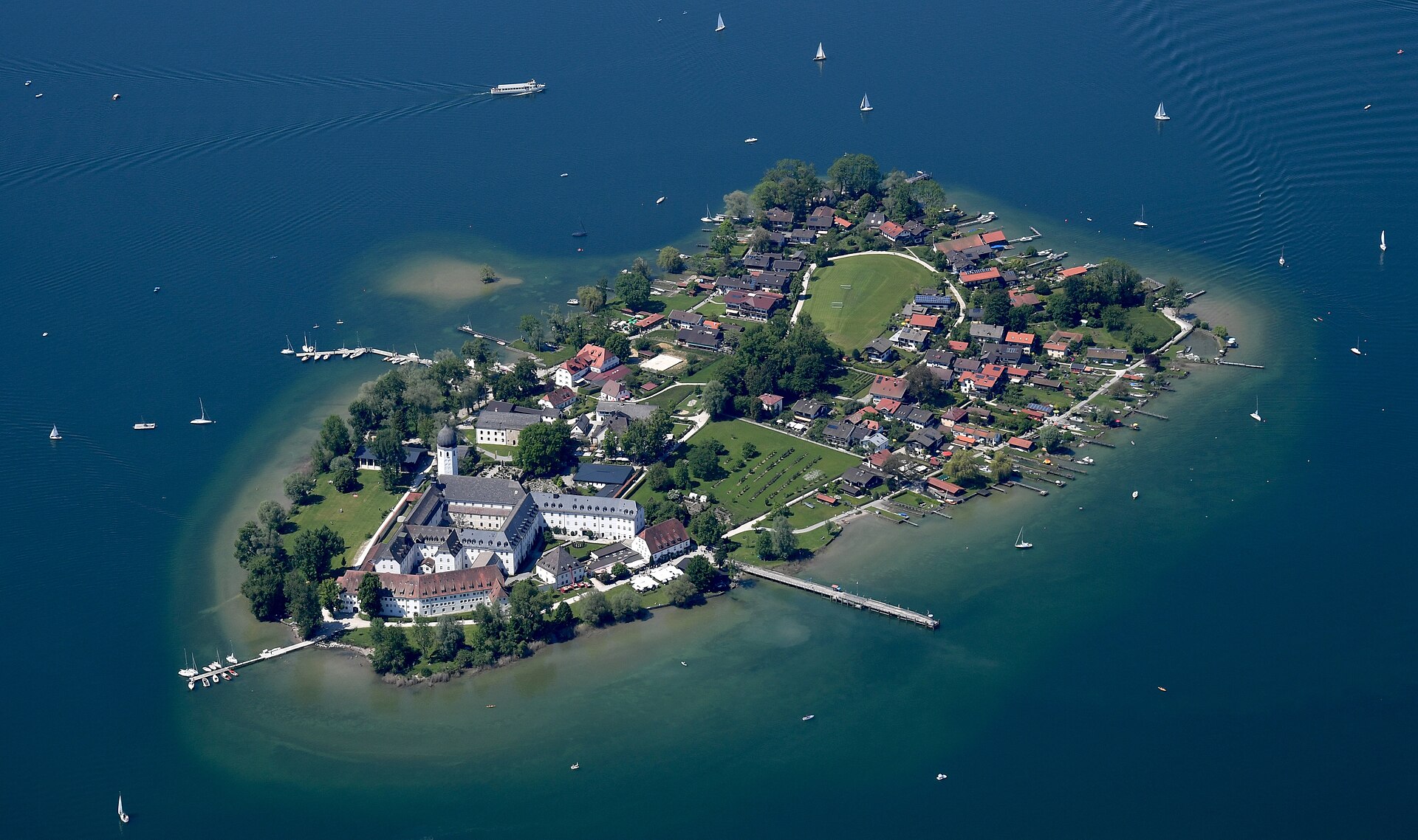Fraueninsel sits in the blue Chiemsee, with its abbey church and onion-domed bell tower beside clustered houses and landing piers.