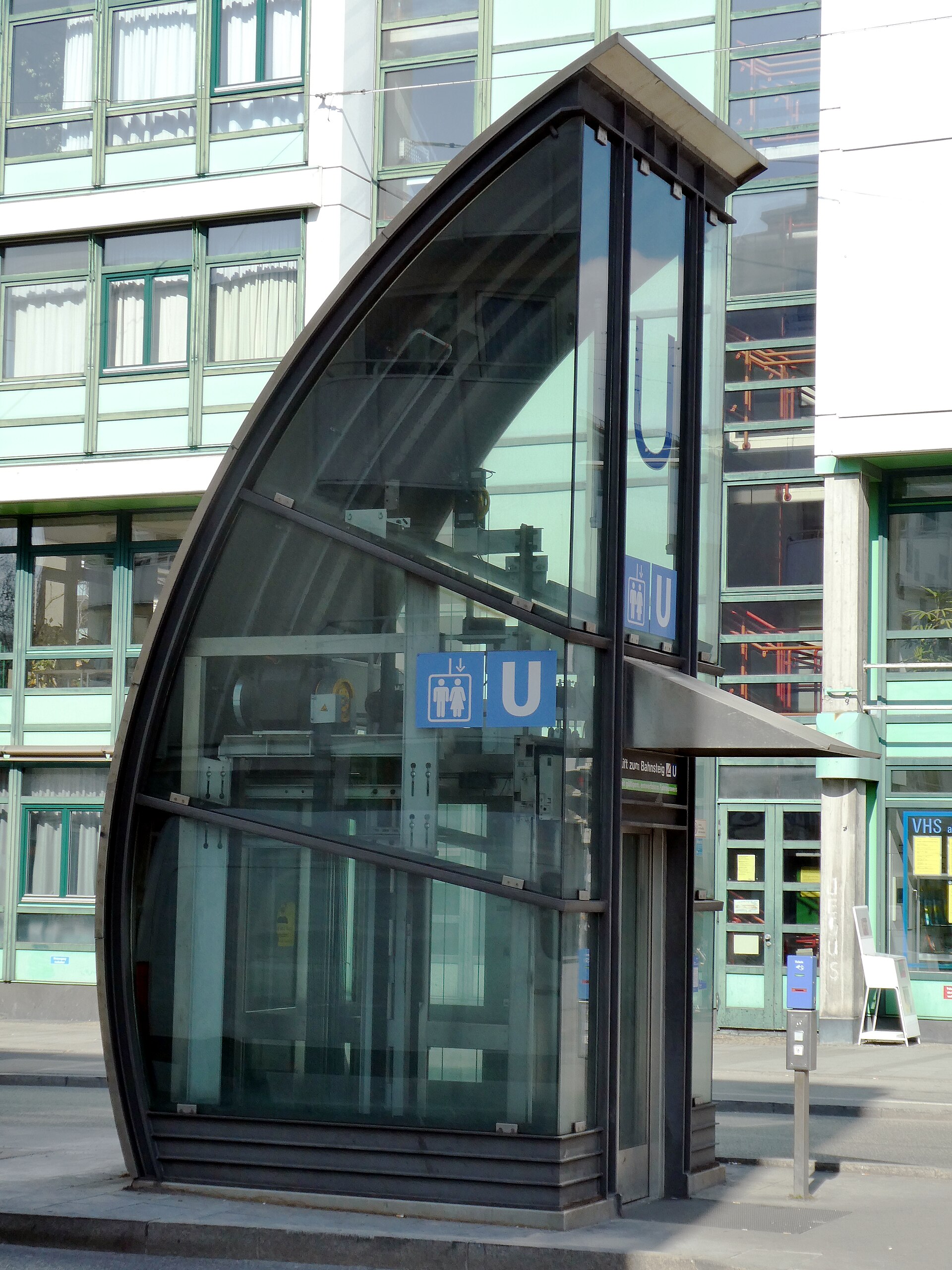 Munich with a Stroller: Accessibility Tips and Family Guide 2 A glass lift entrance at Munich's Harras U-Bahn station has blue underground and elevator signs beside the pavement.