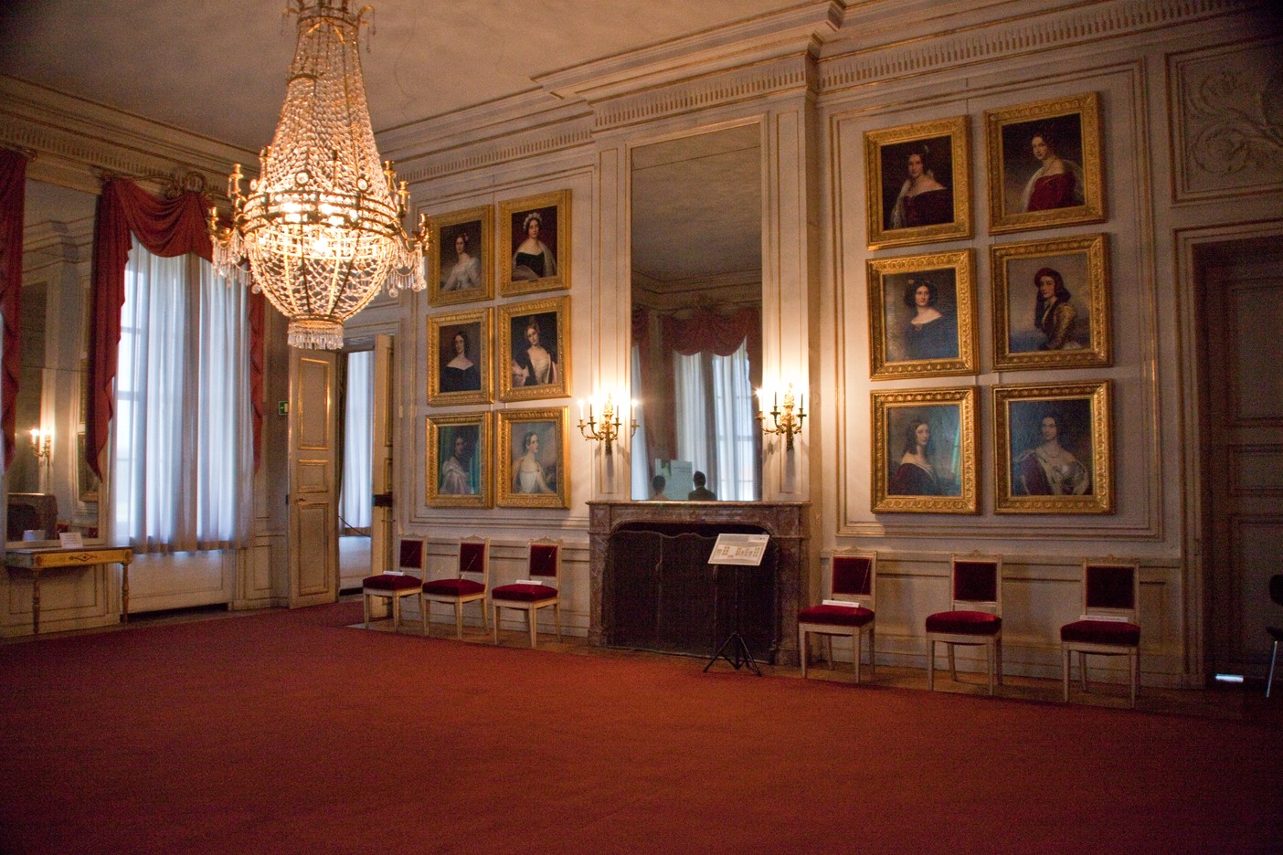 Nymphenburg Palace Munich: Complete Visitor Guide (2026) 2 Gold-framed portraits line the Gallery of Beauties at Nymphenburg Palace in Munich, beneath a crystal chandelier.