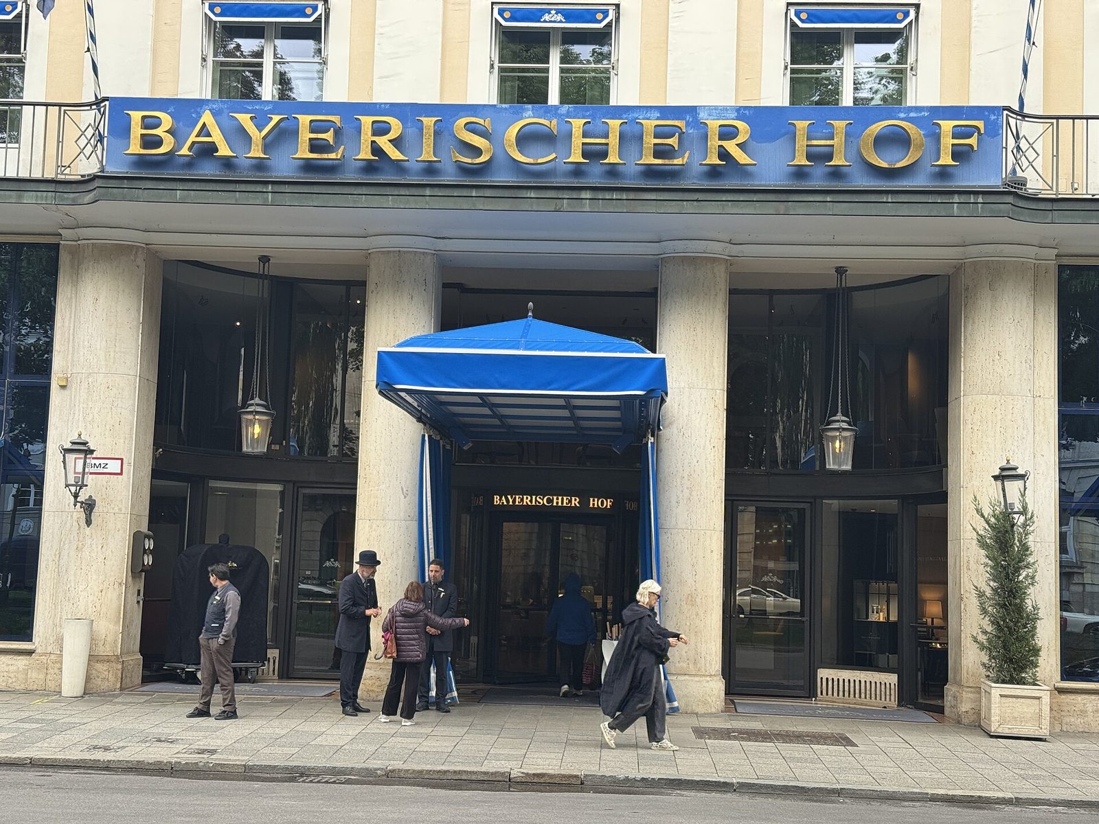 Michelin-Star and Fine Dining in Munich 2 The colonnaded entrance of the Hotel Bayerischer Hof with gold lettering and a blue canopy, people on the pavement