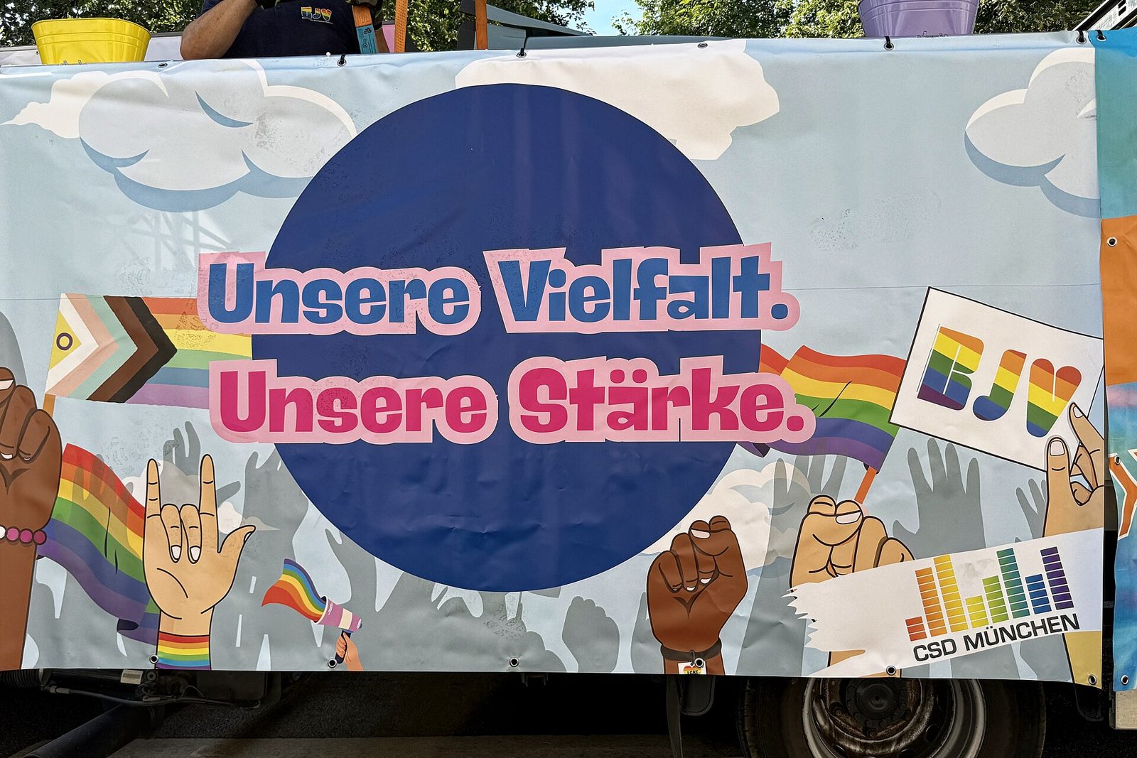 Munich Pride (CSD): Dates, Route and What to Expect 1 A banner on a parade truck reading Unsere Vielfalt. Unsere Stärke. with rainbow flags and raised fists