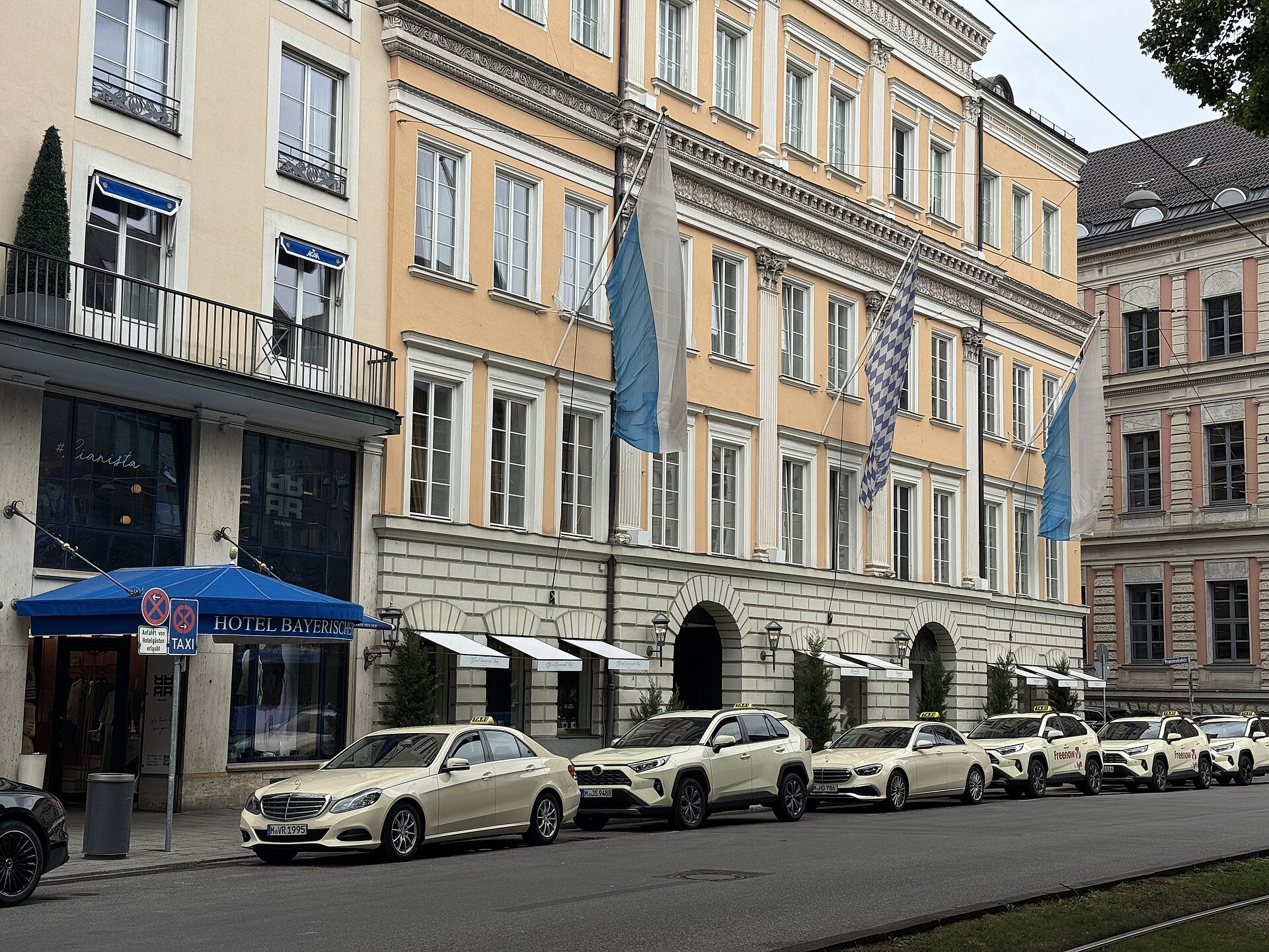 An ornamented wing of Munich’s Bayerischer Hof has tall windows, flags and taxis lined along the street.