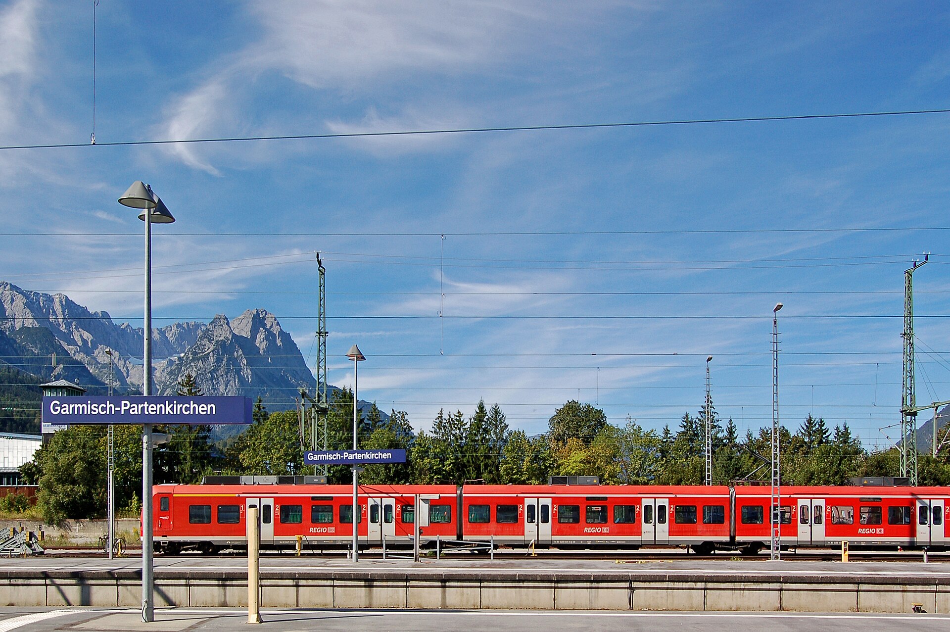 Day Trips from Munich by Train: 15 Best No-Car Excursions 1 A red DB Regio train stands beside Garmisch-Partenkirchen station platforms, with rocky mountains rising behind the station signs.