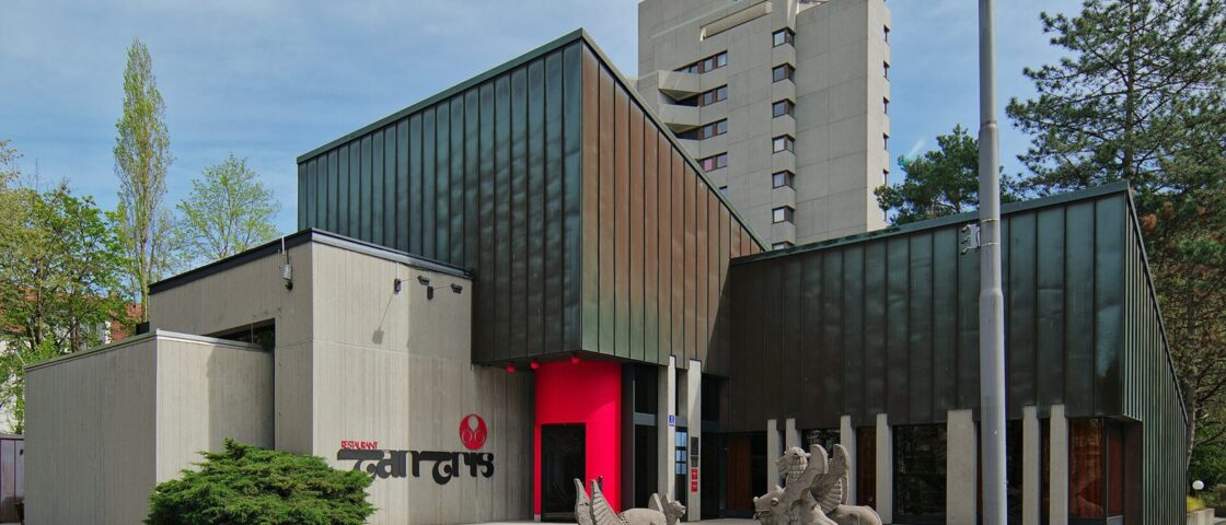 The Tantris restaurant building in Schwabing, a concrete and dark-metal pavilion with a red entrance and stone griffins on the steps