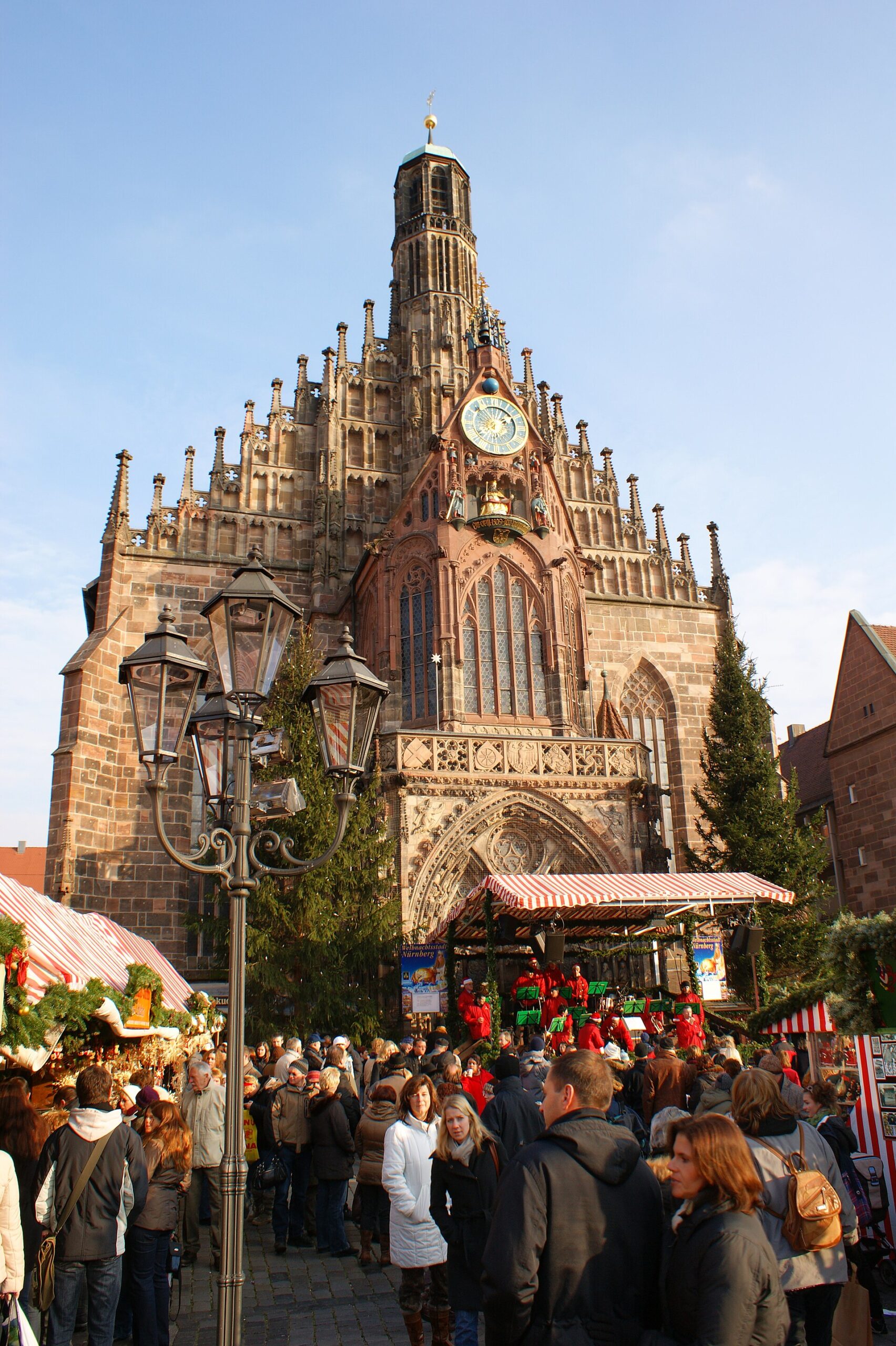 Nuremberg Day Trip from Munich: Complete History and Food Guide 3 Visitors gather among striped Christmas-market stalls beneath the ornate Frauenkirche facade on Nuremberg’s Hauptmarkt.